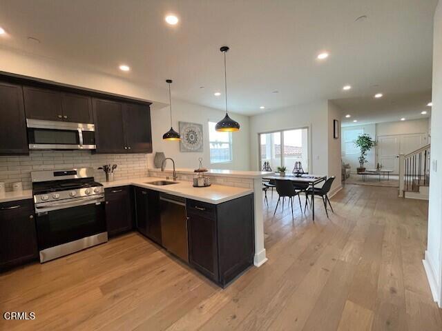 kitchen with light hardwood / wood-style floors, kitchen peninsula, hanging light fixtures, and appliances with stainless steel finishes