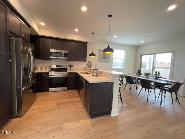 kitchen with kitchen peninsula, appliances with stainless steel finishes, light wood-type flooring, sink, and hanging light fixtures