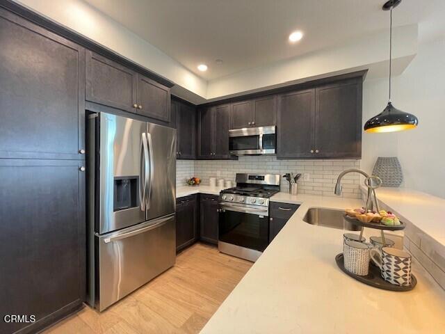 kitchen with sink, hanging light fixtures, tasteful backsplash, appliances with stainless steel finishes, and light wood-type flooring