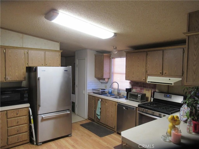 kitchen with vaulted ceiling, light hardwood / wood-style floors, sink, stainless steel appliances, and a textured ceiling