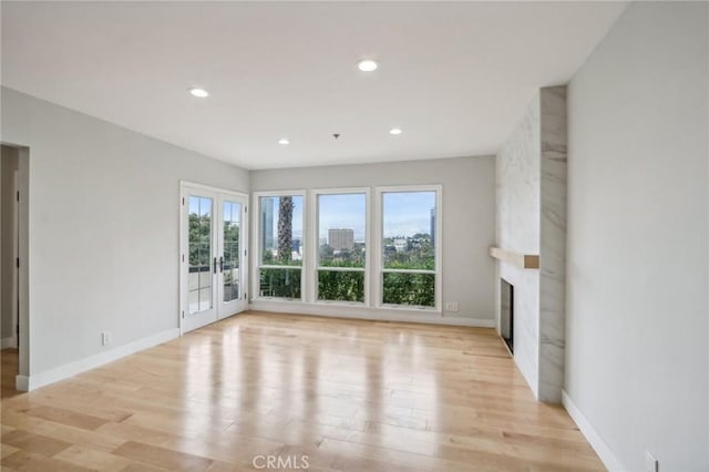 unfurnished living room featuring a fireplace, light hardwood / wood-style floors, and french doors