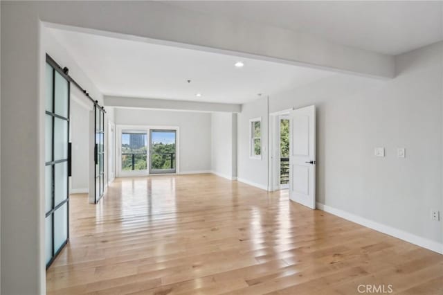 unfurnished room featuring a wealth of natural light, light hardwood / wood-style flooring, and a barn door