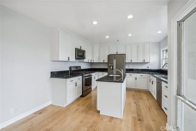 kitchen with light hardwood / wood-style floors, a center island with sink, sink, appliances with stainless steel finishes, and white cabinets