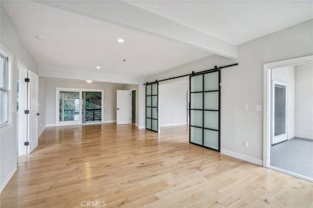 spare room with light hardwood / wood-style floors, beamed ceiling, and a barn door