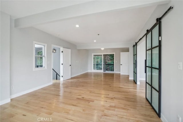 empty room featuring plenty of natural light, light hardwood / wood-style flooring, and a barn door