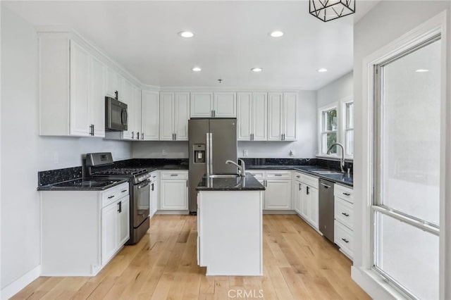 kitchen featuring light hardwood / wood-style floors, an island with sink, appliances with stainless steel finishes, pendant lighting, and white cabinets