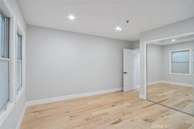 unfurnished bedroom featuring light hardwood / wood-style floors, multiple windows, and a closet