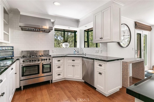 kitchen featuring appliances with stainless steel finishes, dark hardwood / wood-style flooring, sink, wall chimney range hood, and white cabinets