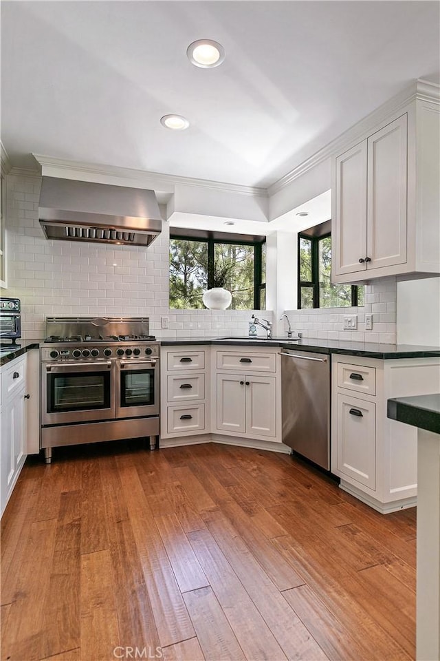 kitchen featuring wall chimney exhaust hood, white cabinetry, appliances with stainless steel finishes, and light hardwood / wood-style flooring