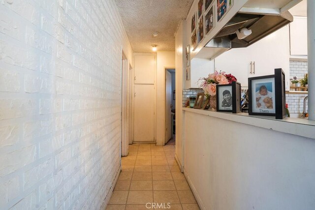 corridor with a textured ceiling, light tile flooring, and brick wall