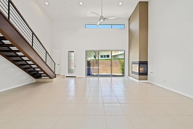 unfurnished living room featuring a towering ceiling, a multi sided fireplace, ceiling fan, and light tile patterned floors