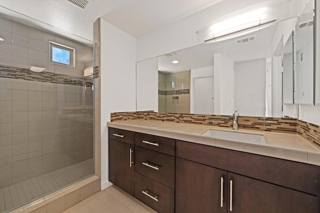 bathroom with a shower with door, tile patterned floors, tasteful backsplash, and vanity