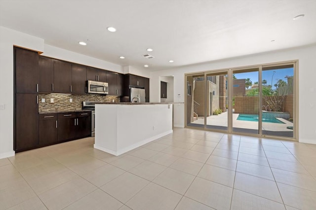 kitchen with stainless steel appliances, light tile patterned floors, tasteful backsplash, dark brown cabinets, and a center island with sink