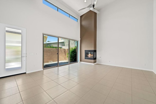 unfurnished living room with a towering ceiling, ceiling fan, and light tile patterned floors