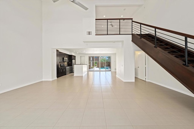 unfurnished living room with a high ceiling, ceiling fan, and light tile patterned floors