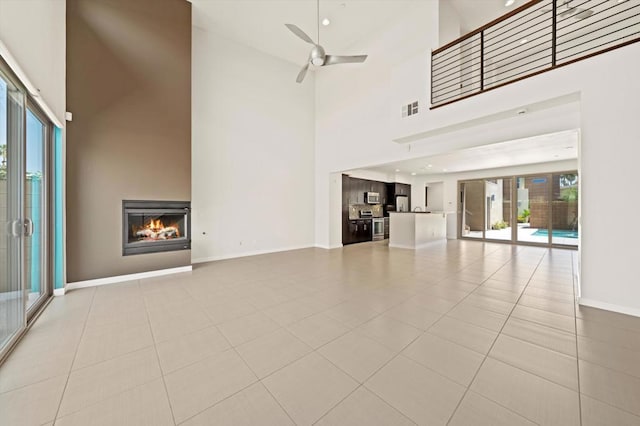 unfurnished living room featuring a towering ceiling, ceiling fan, and light tile patterned floors