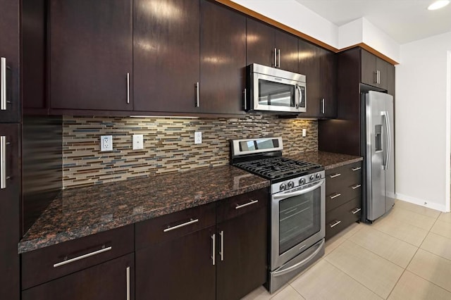 kitchen with stainless steel appliances, light tile patterned floors, dark stone counters, dark brown cabinets, and backsplash