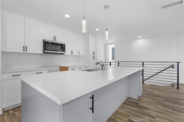 kitchen with dark hardwood / wood-style floors, a center island with sink, white cabinetry, sink, and pendant lighting