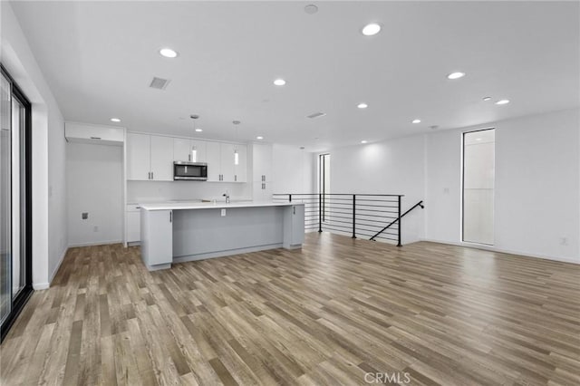 kitchen with white cabinetry, an island with sink, light wood-type flooring, sink, and a breakfast bar