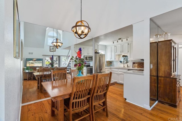 dining area with a notable chandelier, track lighting, sink, and light wood-type flooring