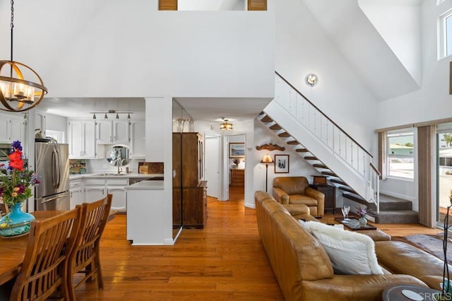 living room with high vaulted ceiling, sink, light hardwood / wood-style flooring, and a notable chandelier