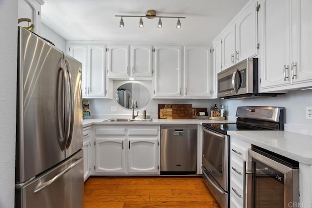 kitchen with light wood-type flooring, stainless steel appliances, white cabinets, wine cooler, and sink