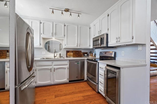 kitchen featuring stainless steel appliances, wine cooler, hardwood / wood-style floors, track lighting, and sink