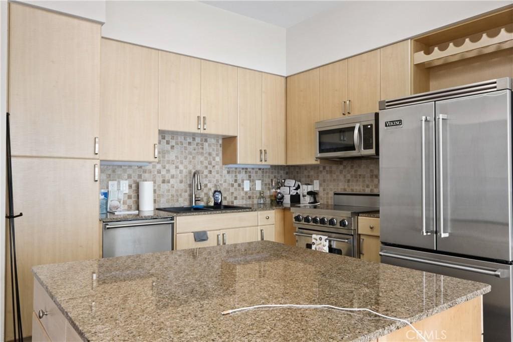 kitchen with decorative backsplash, sink, high quality appliances, light brown cabinets, and light stone counters