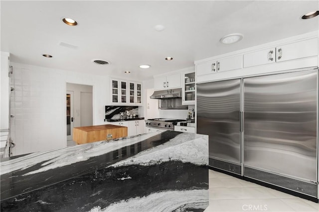 kitchen featuring stainless steel built in fridge, white cabinets, glass insert cabinets, under cabinet range hood, and range