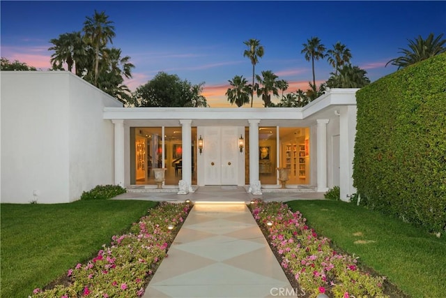 entrance to property with stucco siding, a porch, and a yard