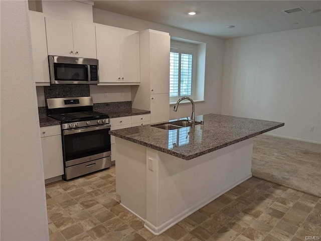 kitchen featuring white cabinetry, sink, stainless steel appliances, an island with sink, and light colored carpet