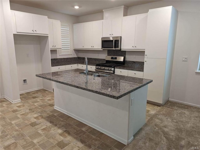 kitchen featuring white cabinets, appliances with stainless steel finishes, dark stone countertops, and an island with sink