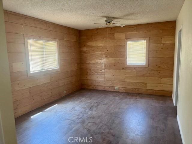 empty room featuring wood walls, a healthy amount of sunlight, and dark hardwood / wood-style flooring