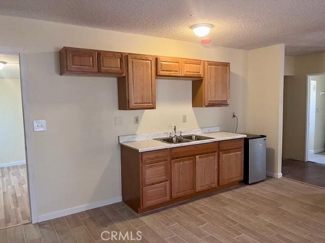 kitchen featuring a textured ceiling, stainless steel fridge, sink, and light hardwood / wood-style flooring