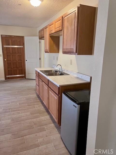 kitchen featuring stainless steel fridge, sink, light hardwood / wood-style floors, and a textured ceiling