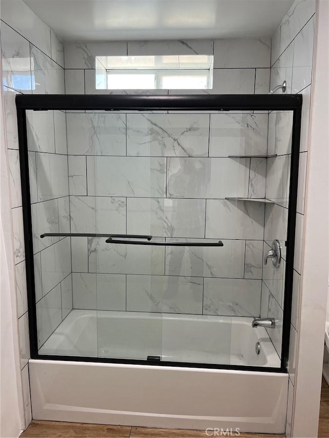 bathroom featuring wood-type flooring and bath / shower combo with glass door