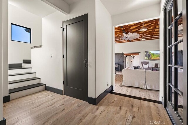 hall featuring beamed ceiling, a healthy amount of sunlight, and light hardwood / wood-style flooring