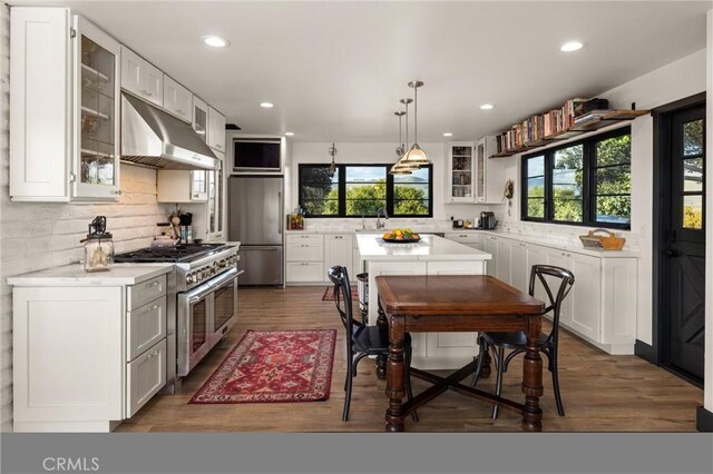 kitchen with exhaust hood, a healthy amount of sunlight, backsplash, and appliances with stainless steel finishes