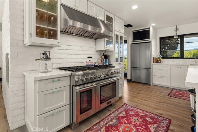 kitchen featuring white cabinetry, brick wall, stainless steel appliances, hardwood / wood-style flooring, and backsplash