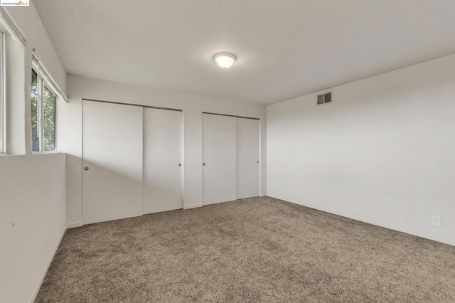 unfurnished bedroom featuring carpet flooring and multiple closets