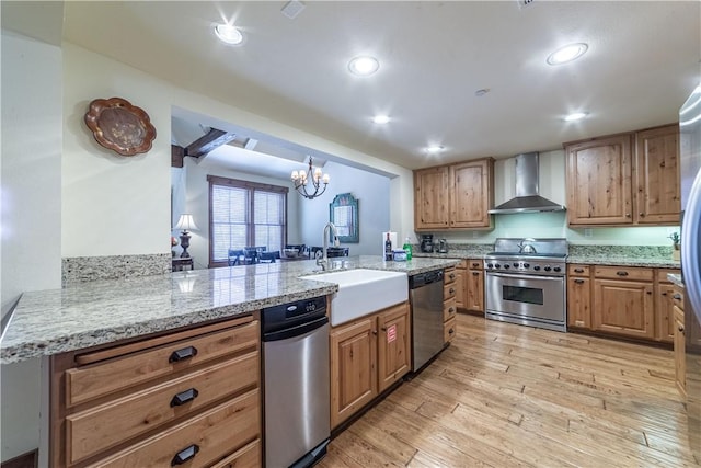 kitchen with kitchen peninsula, appliances with stainless steel finishes, wall chimney exhaust hood, sink, and light hardwood / wood-style floors