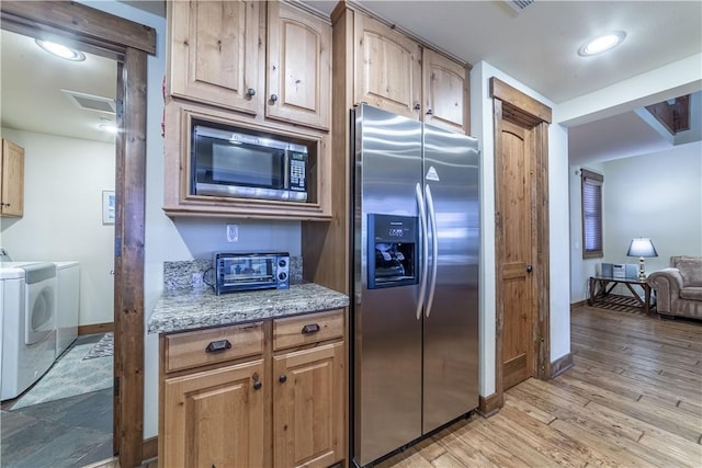 kitchen featuring independent washer and dryer, light stone countertops, light wood-type flooring, and appliances with stainless steel finishes