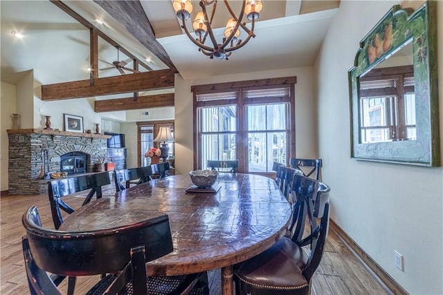 dining area featuring light hardwood / wood-style floors, a stone fireplace, a wealth of natural light, and an inviting chandelier