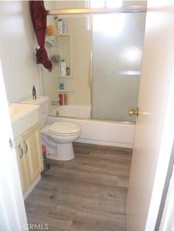 full bathroom with toilet, combined bath / shower with glass door, hardwood / wood-style flooring, and vanity