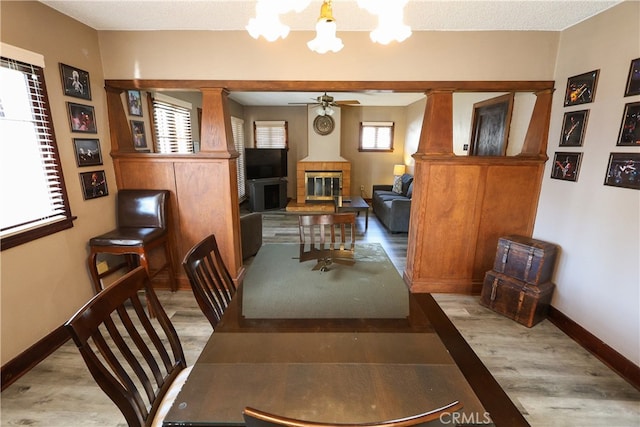 dining space with ceiling fan with notable chandelier, light wood-type flooring, and a large fireplace