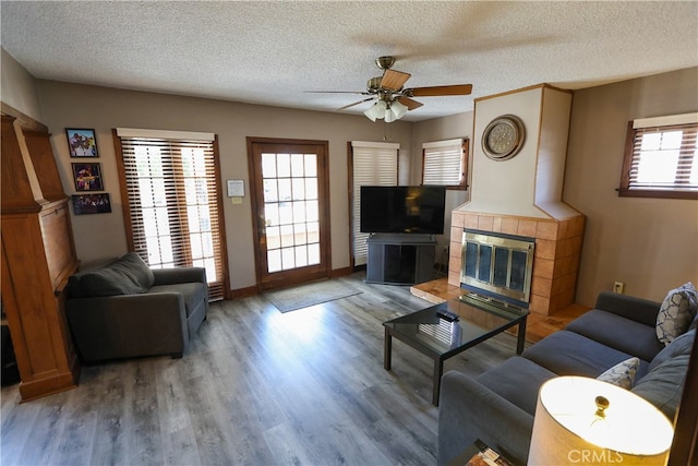 living room with ceiling fan, a tile fireplace, hardwood / wood-style floors, and a textured ceiling