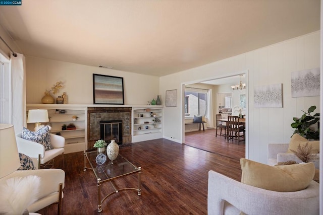 living room featuring an inviting chandelier, dark wood-type flooring, and a brick fireplace