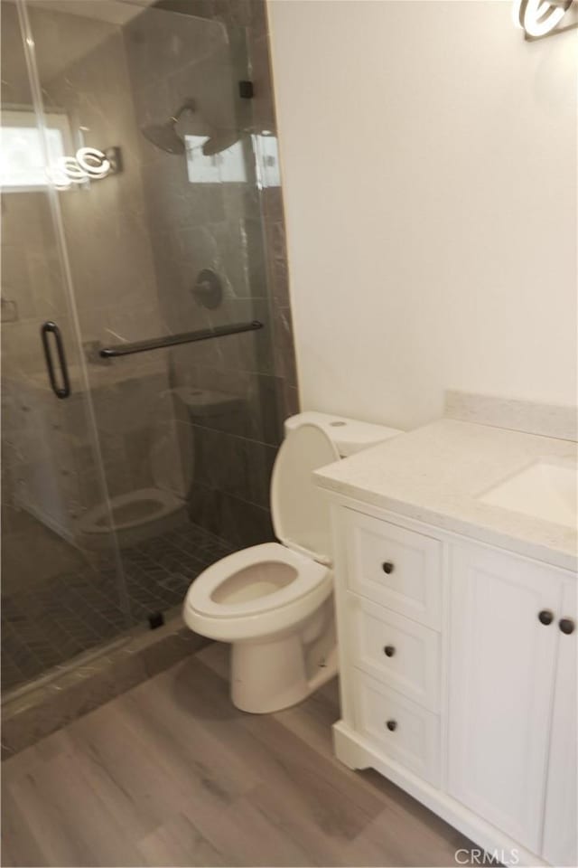 bathroom featuring hardwood / wood-style floors, vanity, toilet, and a shower with door