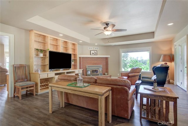 living room featuring dark hardwood / wood-style flooring, a fireplace, a raised ceiling, and ceiling fan