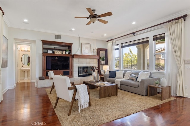 living room featuring a tiled fireplace, crown molding, dark hardwood / wood-style floors, and built in shelves